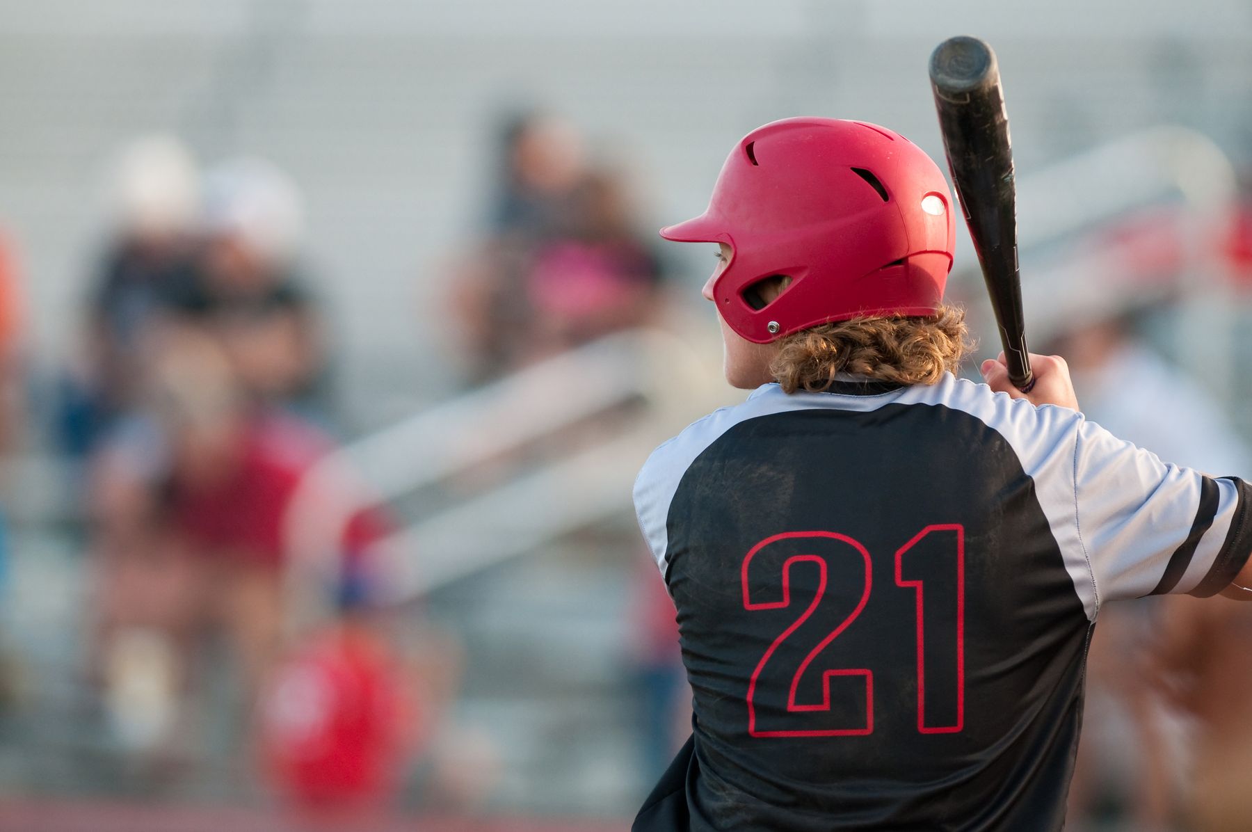 High school hitter in a red helmet and number 21 jersey waiting on a pitch
